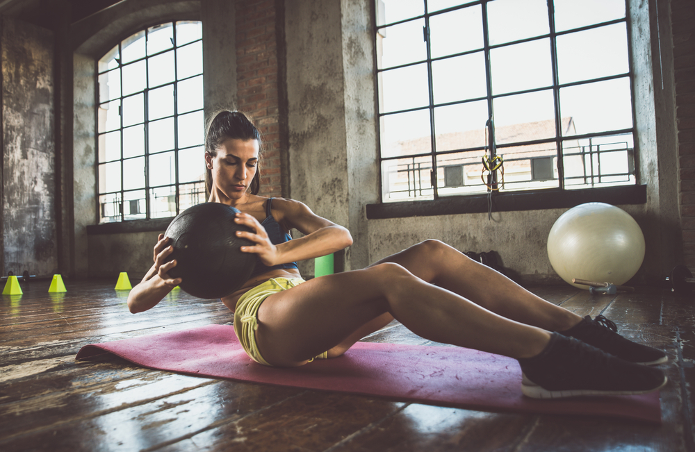 en kvinna som tränar styrka med en medicinboll på ett gym